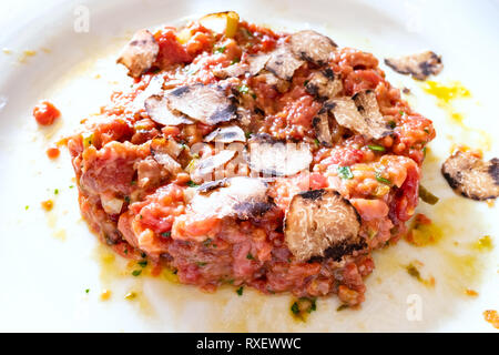 beef steak tartare with raw egg and sliced truffle close up on white plate in Lombardy Stock Photo