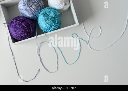 Top view of yarn balls in a wood box. Love word designed from colorful knitting wools strands on white table background. Stock Photo