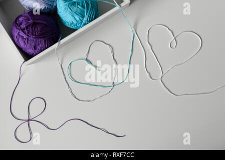 View from above on creative designed hearts from colorful wool strands coming out of the white box with knitting yarn balls. Stock Photo