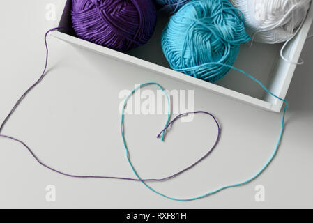 Heart symbol designed from colorful threads out of white box with knitting yarn balls. Stock Photo