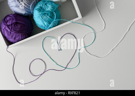 Creative and romantic way of design a love word with heart on white background from colorful threads coming out from wood box with knitting wools. Stock Photo