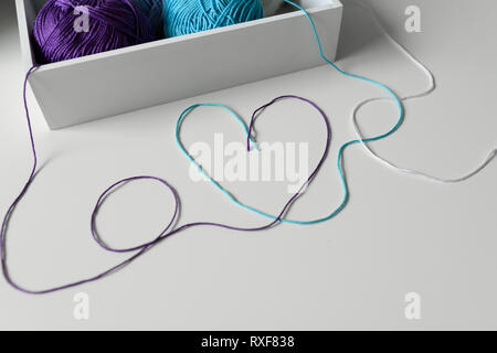 Love word and heart designed from colorful wool threads on white table from knitting yarn in a wood box. Stock Photo