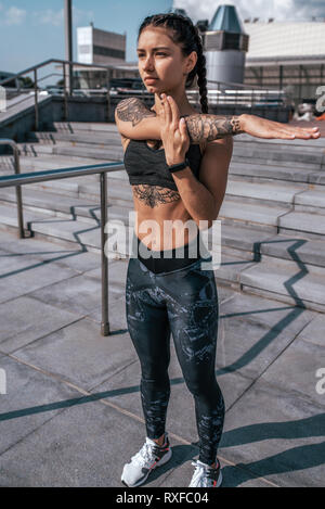 Girl athlete, summer city. Resting after playing sports on street. In  leggings and swimsuit. Woman with tattoos. He looks into the distance,  covers Stock Photo - Alamy