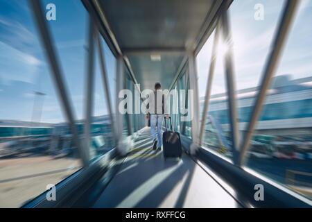 Man hurrying at airport. Rear view of passenger with luggage walking to terminal. Stock Photo