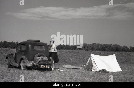 1930s, historical, a young man has a shave standing next to a car of the era (with a GB sticker) parked in a open field next to a small tent, in the Sudentenland, Czechoslovakia. Stock Photo