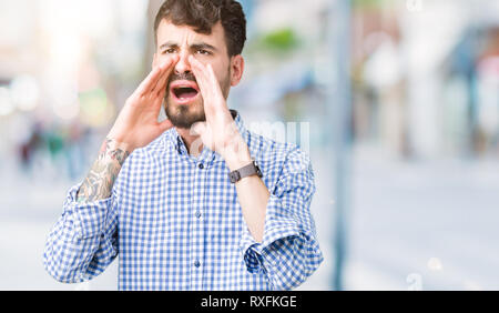 Young handsome business man over isolated background Shouting angry out loud with hands over mouth Stock Photo