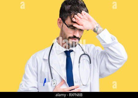 Young doctor man wearing hospital coat over isolated background Touching forehead for illness and fever, flu and cold, virus sick Stock Photo