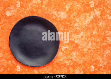 black ceramic plate with an irregular edge on an orange amate bark paper   with a copy space Stock Photo