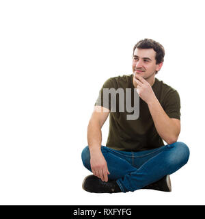 Handsome cheerful young man wearing casual jeans and t-shirt, sitting on floor relaxed with crossed legs, looking away thinking, hand under chin isola Stock Photo