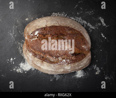 whole bread loaf and scattered white flour on dark background Stock Photo