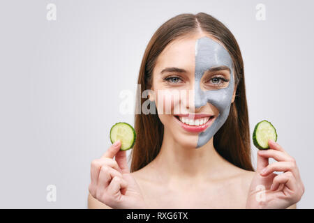 Young woman with clay facial mask holding cucumber slices isolated on white background Stock Photo