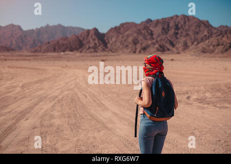 Tourist woman with backpack wearing scarf on head. Traveler admiring Sinai Desert and mountains Stock Photo