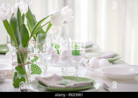 Decor and table setting of the Easter table is a vase with white tulips and dishes of green and white color. Easter decor with white polka dots. Selec Stock Photo
