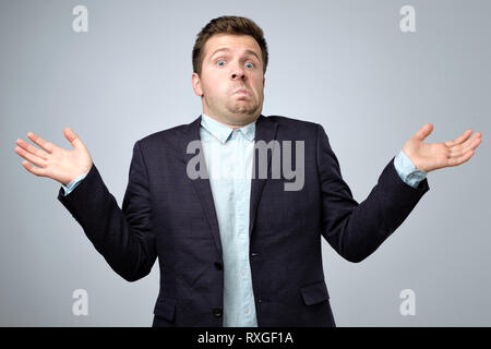 Confused young caucasian man in suit shrugging his shoulders. I do not know what to do in this situation. Stock Photo