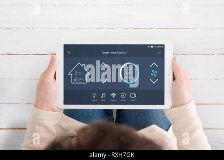 Modern, automated home control app with artificial intelligence on tablet display in woman hands. Top view. Wooden floor in background. Stock Photo