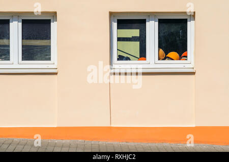 Pile of Orange Construction Helmets On the Windowsill Inside the Building. . Exterior of a Plastered Building on a Sunny Day. Copy Space Stock Photo