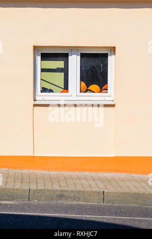Pile of Orange Construction Helmets On the Windowsill Inside the Building. . Exterior of a Plastered Building on a Sunny Day. Copy Space Stock Photo