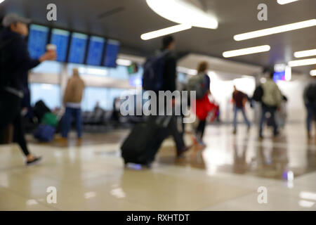 Defocus blurred bokeh of travelers in airport terminal traveling for work and vacation - suitcases, luggage, backpacks, digital flight schedule board