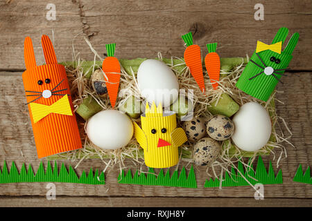 Easter holiday concept with eggs, cute handmade bunny, chicks in papaer box for egg on wooden table, sptingtime background Stock Photo