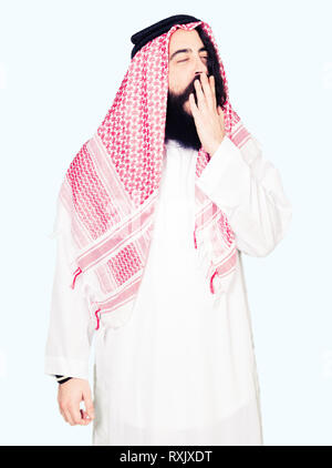 Arabian business man with long hair wearing traditional keffiyeh scarf bored yawning tired covering mouth with hand. Restless and sleepiness. Stock Photo