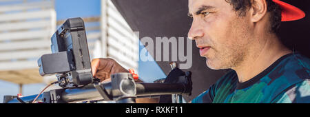 Steadicam operator and his assistant prepare camera and 3-axis stabilizer-gimbal for a commercial shoot. BANNER, LONG FORMAT Stock Photo