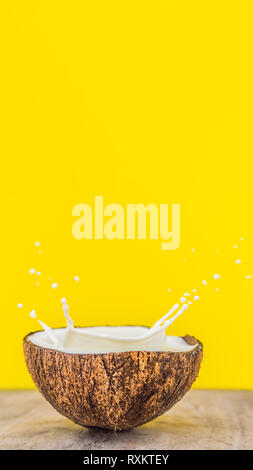 Coconut fruit and milk splash inside it on yellow background VERTICAL FORMAT for Instagram mobile story or stories size. Mobile wallpaper Stock Photo