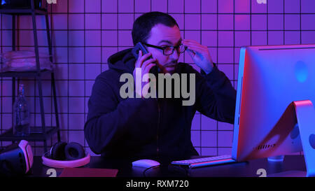 Coding specialist in casual with computer and talking by phone while coding information to create convenient software. Stock Photo