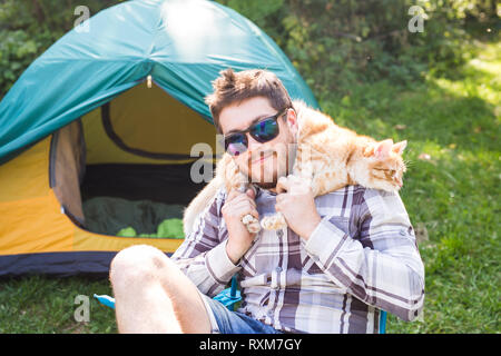 People, tourism and nature concept - Man in sunglasses holding cat on shoulders Stock Photo