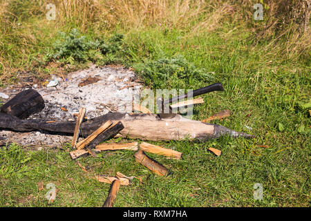 A pile of logs for a fire with a long handled axe embedded in a log ready for use Stock Photo