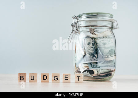 us dollars bill in glass jar and word budget made of wooden blocks Stock Photo