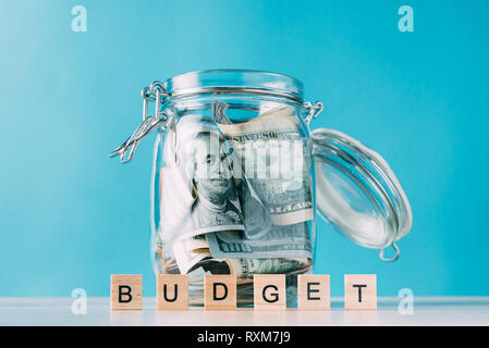 glass jar filled with dollar banknotes and word budget made of wooden blocks on blue background Stock Photo