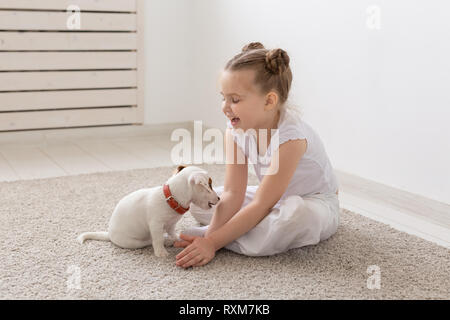 People, pets and animal concept - Little girl sitting on the floor over white background and holding puppy Jack Russell Terrier Stock Photo