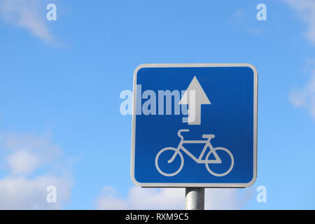 Bicycle road sign isolated on blue sky. White bicycle symbol on the blue square with arrow, the bike lane Stock Photo