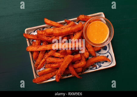 Portion of deep fried sweet potato chips or fries with dipping sauce on plate over table, elevated top view, directly above Stock Photo