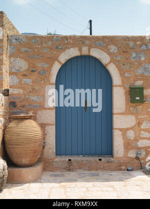 Very well maintained vibrant wooden curved door on stone wall  and green postal box in Greek village. Stock Photo