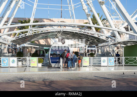 family queuing up at box office of ferris wheel to buy tickets to go on a ride at V&A Waterfront, Cape Town, South Africa in Winter at sunset Stock Photo