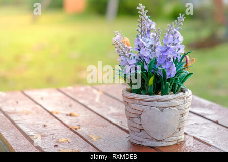 Artificial lavender flowers in metal vase on wood table with sunshine backlit. Stock Photo
