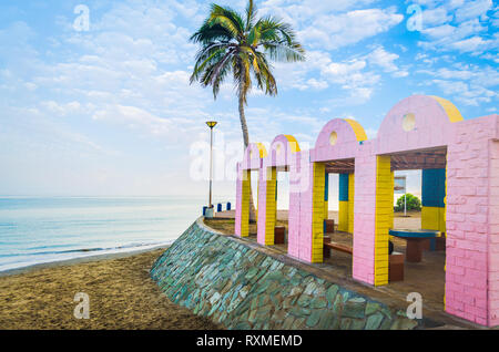 Beach Resting Place with pink and yellow bricks with calm sea and a lone coconut tree in the background. From Muscat, Oman. Stock Photo