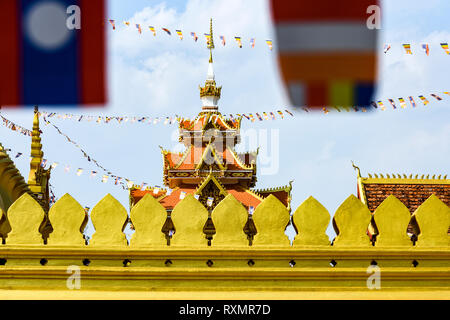 (selective focus) Stunning view of the beautiful Wat That Luang Neua with some blurred Laos flags waving in the foreground.