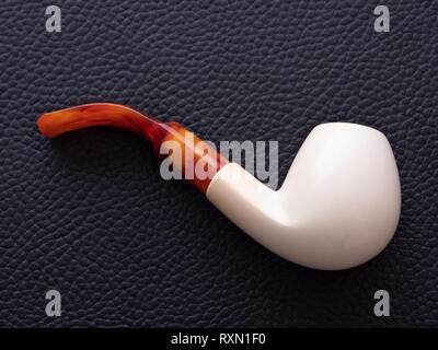 An Elegant and Simple White Meerschaum Pipe with an Amber Mouthpiece on a Black Leather Background Stock Photo