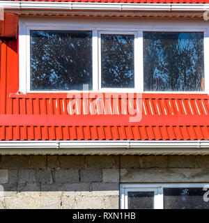 House with plastic windows and a red roof of corrugated sheet. Roofing of metal profile wavy shape on the house with plastic windows. House of cinder  Stock Photo