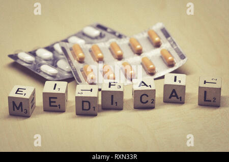 wooden cubes showing the word medical on a table, pills in background Stock Photo