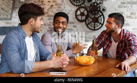 Young men talking, eating chips and drinking beer Stock Photo