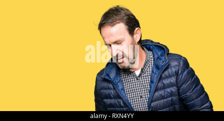 Middle age handsome man wearing winter coat with hand on stomach because nausea, painful disease feeling unwell. Ache concept. Stock Photo