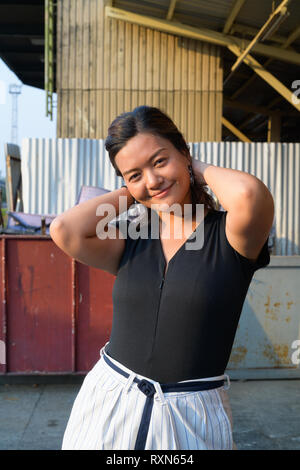 Young happy Asian woman pushing hair back in urban street Stock Photo