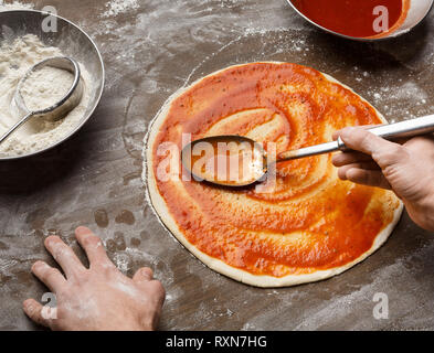 Man spreading tomato paste on pizza base Stock Photo