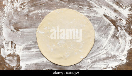 Raw rolled out pizza dough on floured surface Stock Photo