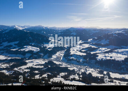 View from a drone on a winter mountains covered with forests and snow in Alps and small villages in the distance. Stock Photo