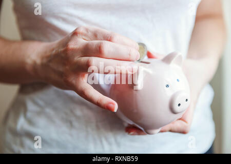 Female woman hands holding pink piggy bank and putting money Euro coin. Saving investment budget business wealth retirement financial money banking concept Stock Photo