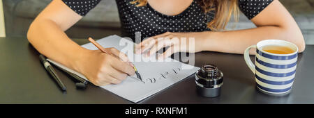 Calligrapher Young Woman writes phrase on white paper. Bible phrase about love Inscribing ornamental decorated letters. Calligraphy, graphic design Stock Photo